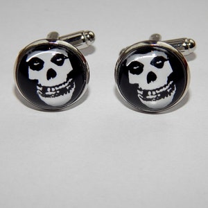 以下が含まれることがあります： 黒と白の頭蓋骨の画像がそれぞれに施された、銀製のカフスボタンのペアです。