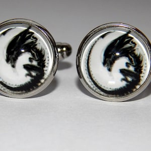 May include: A pair of silver cufflinks with a black and white image of an alien creature inside a circular glass dome.