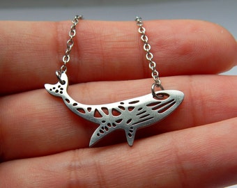 May include: A silver necklace with a whale pendant. The whale is made of metal and has a cutout design.