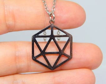 May include: A silver chain necklace with a geometric pendant. The pendant is a hexagonal shape with a black metal finish and a geometric design.