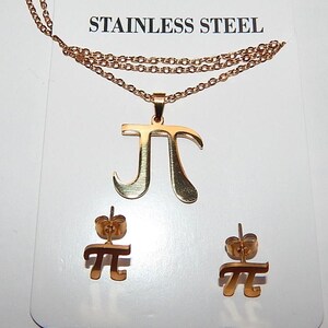Pode incluir: Um conjunto de joias em aço inoxidável em tom de ouro rosa, composto por um colar com um pendente do símbolo pi e dois brincos a condizer. O conjunto é apresentado num cartão branco com o texto STAINLESS STEEL impresso.