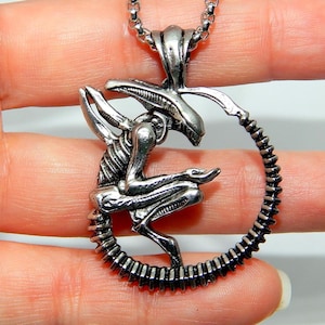 May include: Silver-toned pendant necklace featuring a detailed Xenomorph alien design. The pendant depicts the creature within a circular frame, suspended from a chain. The necklace is a sci-fi themed accessory.
