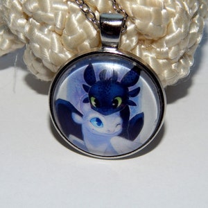 May include: A silver necklace with a round glass pendant featuring a cartoon image of two dragons, one black and one white, with their heads touching.
