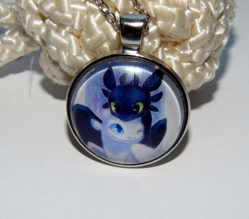 May include: A silver necklace with a round glass pendant featuring a cartoon image of two dragons, one black and one white, with their heads touching.