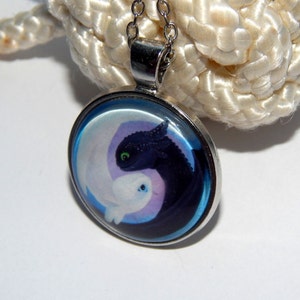 May include: A silver necklace with a round glass pendant featuring a black and white dragon design. The dragons are in a yin yang symbol with a blue background.