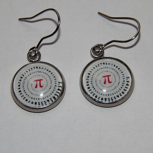 Puede incluir: Un par de pendientes colgantes plateados. Cada pendiente presenta un colgante circular con fondo blanco, un símbolo Pi rojo y una espiral de números. Los pendientes tienen cierre de gancho.