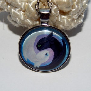May include: A silver necklace with a round glass pendant featuring a black and white dragon design. The dragons are in a yin yang symbol with a blue background.