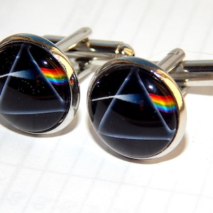 May include: A pair of silver cufflinks with black and white circular designs featuring a rainbow prism. The designs are reminiscent of the album cover for Pink Floyd's "Dark Side of the Moon".