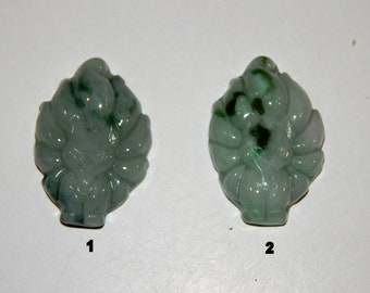 Op de afbeelding: Twee groene jade hangers gegraveerd in de vorm van een negenstaartige vos. De hangers zijn beide ongeveer 5 cm hoog en 2,5 cm breed. De eerste hanger heeft een meer effen groene kleur, terwijl de tweede hanger een meer gevlekte groene kleur heeft.