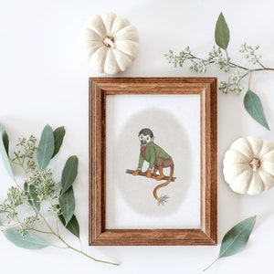 May include: A framed illustration of a monkey wearing a green jacket and a red bow tie, sitting on a branch. The monkey is brown with a white face and a long tail. The illustration is set against a white background.
