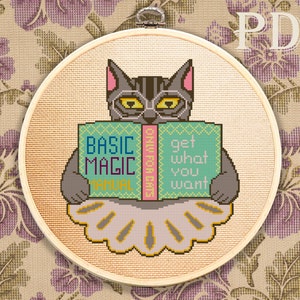 May include: A cross-stitch pattern featuring a black cat wearing a tutu and holding a book titled "Basic Magic Manual: Get What You Want".