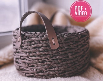 May include: A gray woven basket with a leather handle. The basket is sitting on a white fuzzy surface.