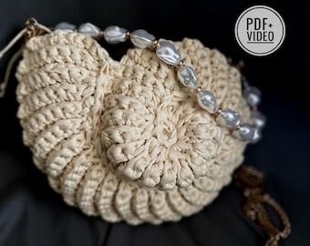 May include: A cream-colored, crocheted handbag with a circular design. The bag is adorned with a strand of large, irregular, off-white pearls. A gold-colored chain and a tag that says "PDF+VIDEO" are also visible.