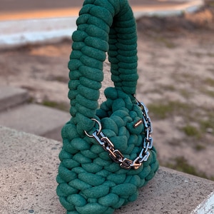 May include: A dark green crocheted handbag with a silver chain strap.