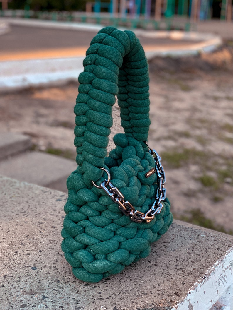 May include: A dark green crocheted handbag with a silver chain strap.
