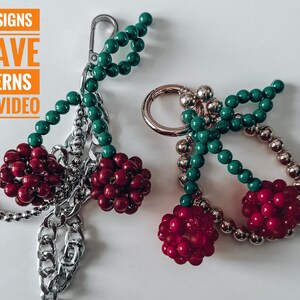 May include: Two beaded keychains with a cherry design. Each keychain features a cluster of red beads, green beads, and silver-colored chain and hardware. The image also includes text that reads "20+ DESIGNS WEAVE PATTERNS ONLY VIDEO."