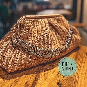 May include: A woven straw clutch bag with a gold chain strap. The bag has a pleated design and is a light beige colour.