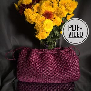 May include: A deep burgundy woven drawstring bag sits in front of a bouquet of yellow and maroon chrysanthemums. The bag has a textured surface and a drawstring closure. A white circle with the text "PDF + VIDEO" is in the background.