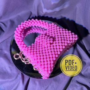 May include: A pink beaded handbag with a gold chain strap. The bag is made of small, round beads and has a unique, modern design.