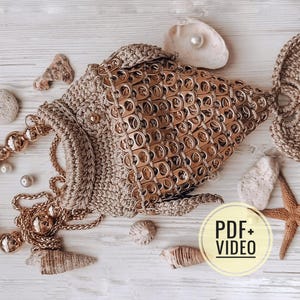 May include: A handmade, beige fish-shaped purse with a beaded handle and a chain strap. The body is made from recycled metal tabs. The purse is decorated with seashells, a starfish, and pearls. A PDF+VIDEO icon is in the image.