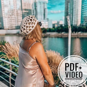May include: A woman wearing a cream-colored crochet beret with a geometric design, paired with a satin slip dress. The image is set against a backdrop of a city skyline and a body of water. A circular graphic with the text "PDF + VIDEO" is in the lower right corner.
