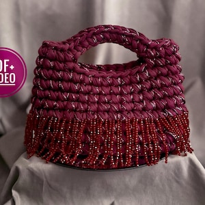 May include: A burgundy crochet handbag with a handle and beaded fringe. The bag is made of thick, textured yarn with silver threads woven throughout. The fringe is made of small, red beads.