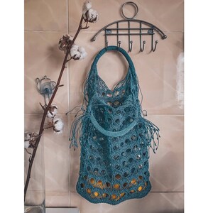 May include: A teal blue crocheted tote bag with fringe hanging from a metal hook rack. The bag is empty.