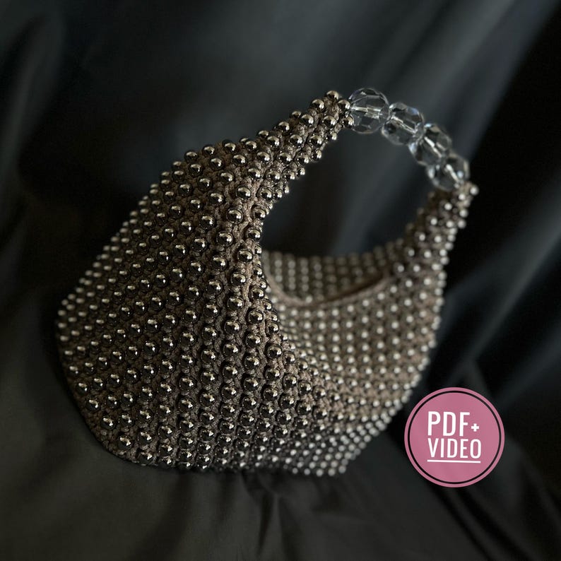May include: A silver beaded handbag with a clear plastic handle. The bag is shaped like a crescent moon and has a textured surface.