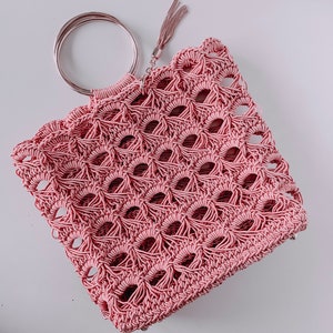 May include: A pink crocheted bag with a silver ring handle and a tassel.