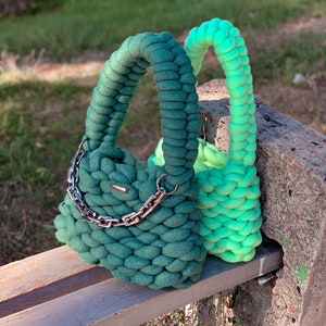 May include: Two crocheted handbags, one green and one ombre green to light green, with a silver chain strap on the green bag.