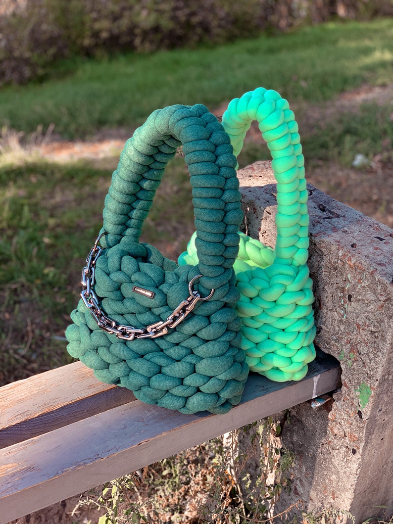 May include: Two crocheted handbags, one green and one ombre green to light green, with a silver chain strap on the green bag.