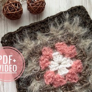 以下が含まれることがあります： 手作りのかぎ針編みの正方形、花の模様。正方形は、ピンクの花びらに囲まれた中央の白い花と、ふわふわのグレーと茶色のボーダーが特徴です。画像には、ピンクの円の中に「PDF + VIDEO」というテキストが含まれています。