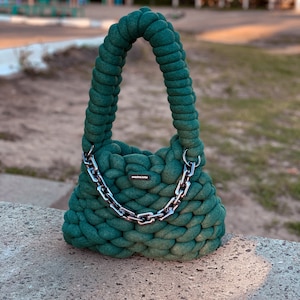 May include: A dark green crocheted handbag with a silver chain strap. The bag has a small label that reads "handmade love".