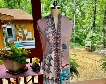 May include: A sleeveless pink dress with a floral and abstract print. The dress has a V-neck and a zipper closure. The dress is on a mannequin in front of a wooden porch.