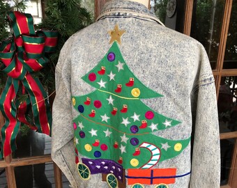 May include: A light blue denim jacket with a Christmas tree embroidered on the back. The tree is green with red and white ornaments, a gold star on top, and a candy cane hanging from a branch. The tree is sitting on a wagon with red and orange boxes and green wheels.