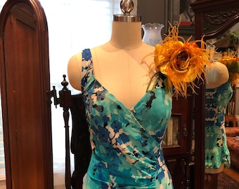 Op de afbeelding: Een blauwe en witte badpak met bloemenprint, een gerimpelde zoom en een grote gele bloem broche.