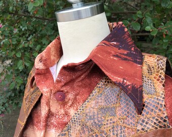 May include: A brown leather vest with a snakeskin pattern and a brown and orange patterned shirt underneath. The vest has a zip fastening and multiple pockets.