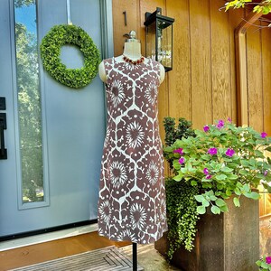 May include: A brown and white patterned sleeveless dress on a mannequin in front of a wooden door and a potted plant.