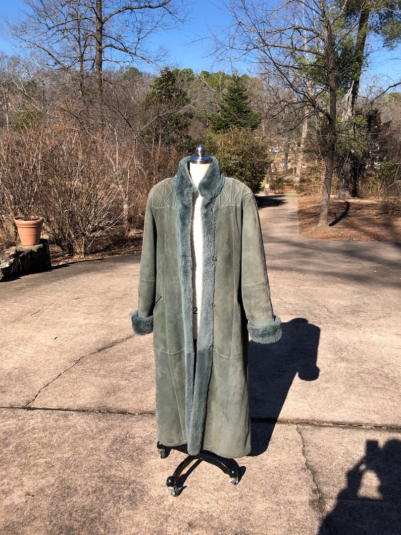 May include: A long, teal-colored suede coat with a fur lining. The coat is on a mannequin and has a button closure.
