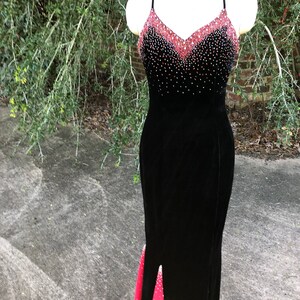 Puede incluir: Un vestido de noche de terciopelo negro con un dise&ntilde;o degradado rojo y negro. El corpi&ntilde;o est&aacute; adornado con pedrer&iacute;a y la falda tiene una peque&ntilde;a abertura en la parte delantera.