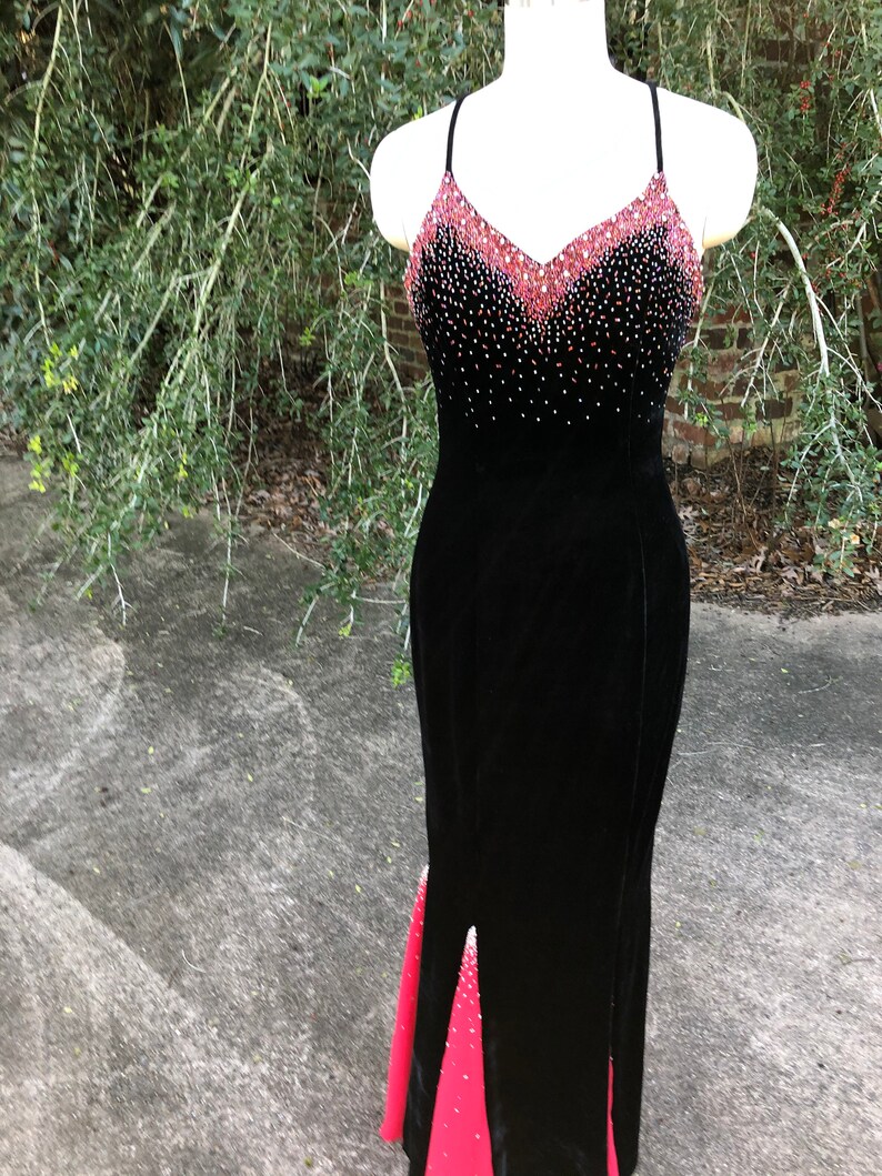 Puede incluir: Un vestido de noche de terciopelo negro con un dise&ntilde;o degradado rojo y negro. El corpi&ntilde;o est&aacute; adornado con pedrer&iacute;a y la falda tiene una peque&ntilde;a abertura en la parte delantera.