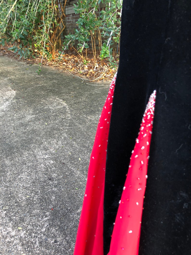 Puede incluir: Un vestido de terciopelo negro con una superposici&oacute;n de sat&eacute;n rojo y adornos plateados. El vestido tiene un corpi&ntilde;o ajustado y una falda fluida.
