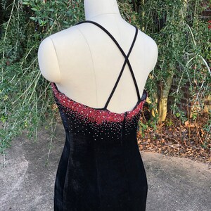 Puede incluir: Vestido de terciopelo negro con un escote de cuentas rojas y una espalda con tirantes cruzados.