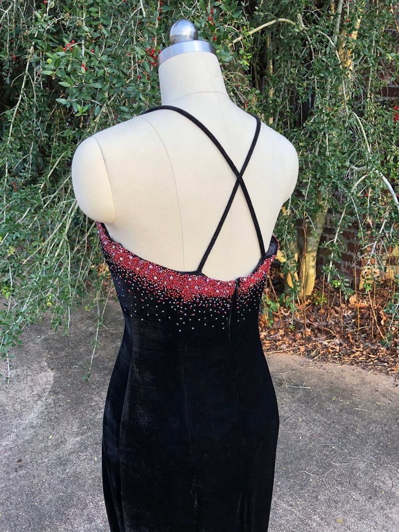 Puede incluir: Vestido de terciopelo negro con un escote de cuentas rojas y una espalda con tirantes cruzados.