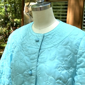 May include: A light blue quilted robe with a button closure. The robe has a floral pattern and is made of a soft, silky fabric.