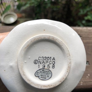 Może przedstawiać: Biały talerz ceramiczny z czarną i białą naklejką na spodzie. Naklejka zawiera napis "C3201A ONAPCO 1958" oraz "National Potteries Co. CLEVELAND, OHIO. MADE IN JAPAN".