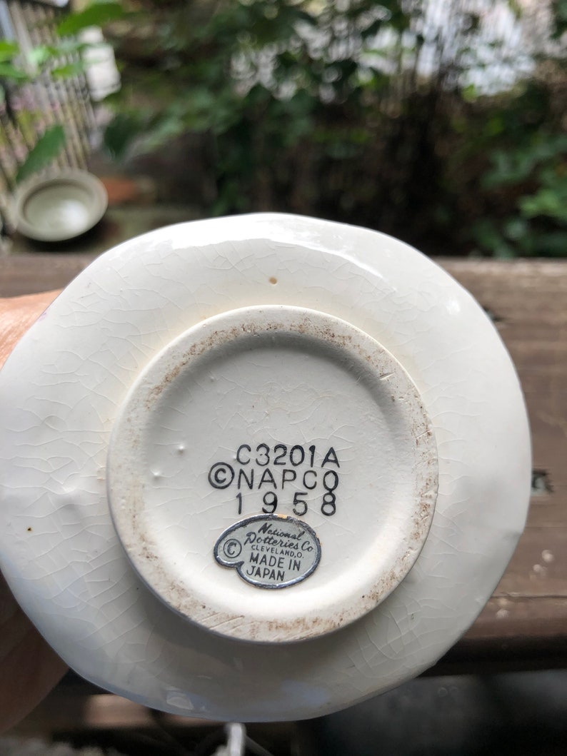 Może przedstawiać: Biały talerz ceramiczny z czarną i białą naklejką na spodzie. Naklejka zawiera napis "C3201A ONAPCO 1958" oraz "National Potteries Co. CLEVELAND, OHIO. MADE IN JAPAN".