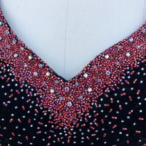 Puede incluir: Un vestido de terciopelo negro con escote en V adornado con cuentas rojas e iridiscentes.