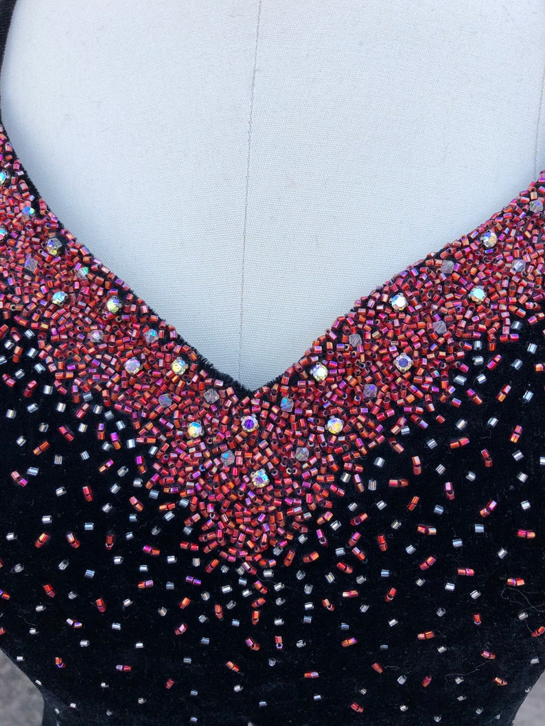 Puede incluir: Un vestido de terciopelo negro con escote en V adornado con cuentas rojas e iridiscentes.