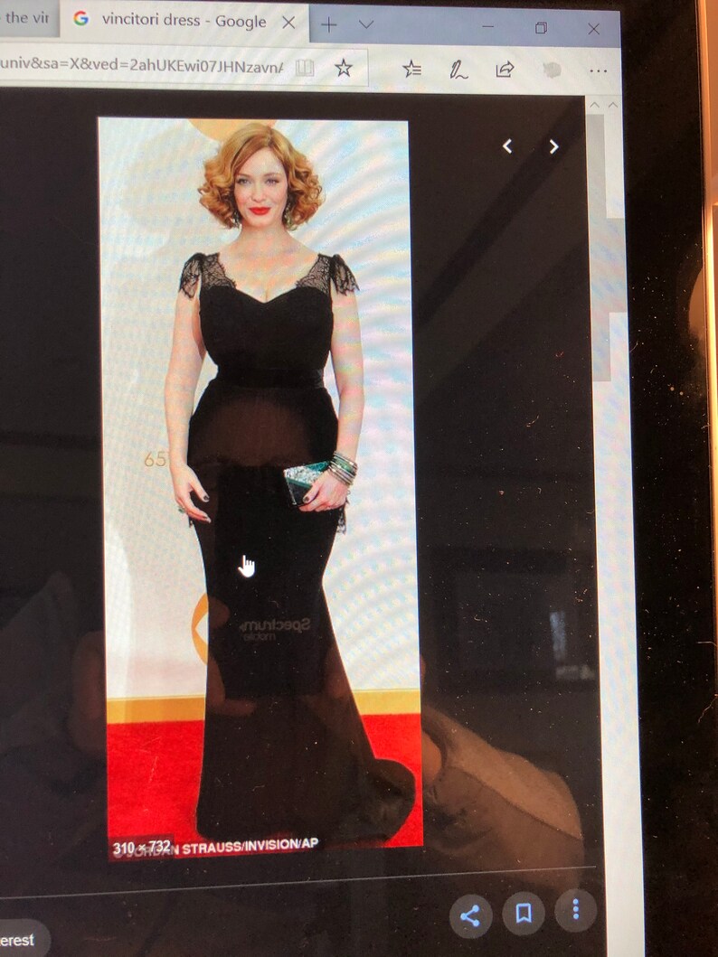 Puede incluir: Una mujer con un vestido negro de manga larga, largo hasta el suelo, con detalles de encaje en los hombros y el escote. Est&aacute; de pie sobre una alfombra roja con un escenario de fondo.